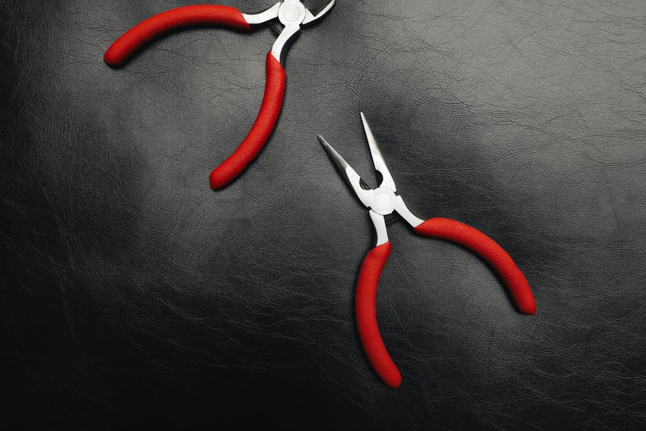 Two red-handled pliers resting on a black leather background in a flat lay style.