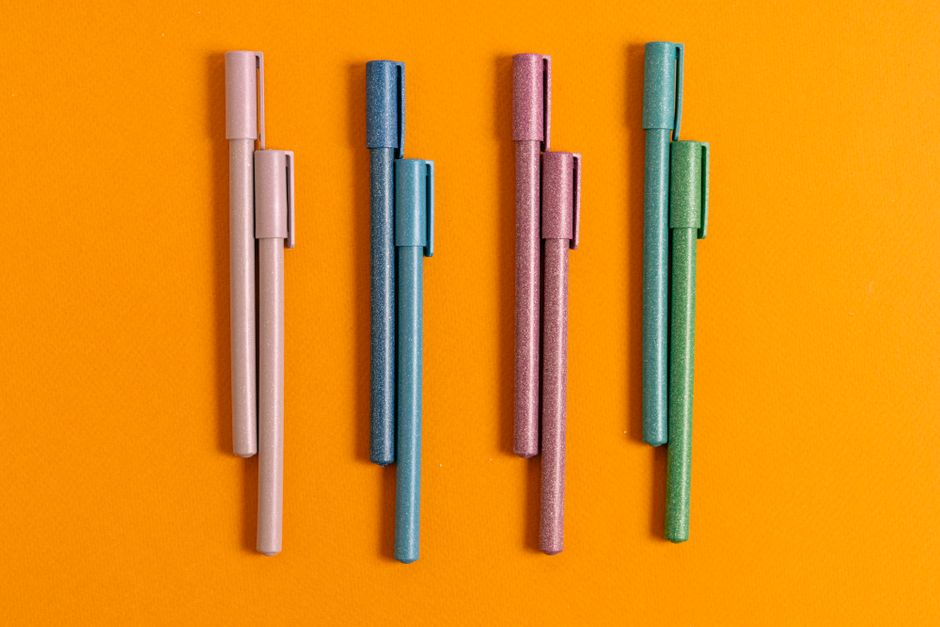 Four colorful pens neatly arranged on a bright orange background. Perfect for stationery enthusiasts.