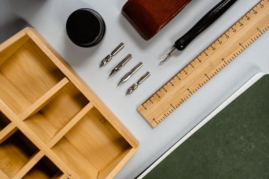 Flat lay of vintage stationery including ink, pen nibs, and a wooden ruler on a desk.