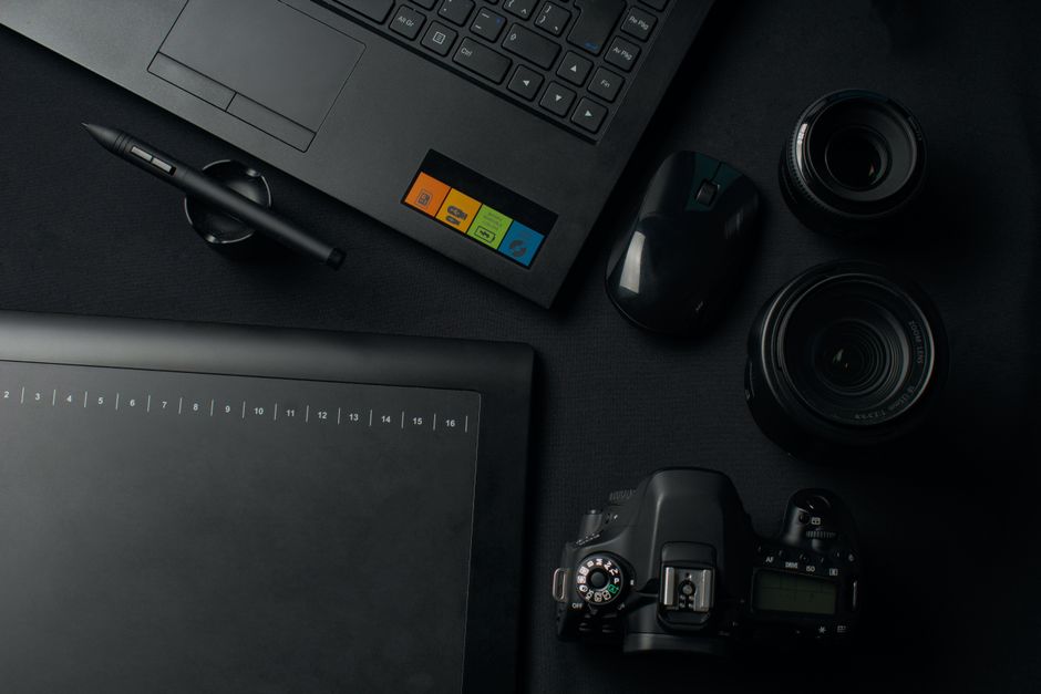 Top view of a modern workspace setup featuring a camera, laptop, graphic tablet, and lenses for photography and editing.