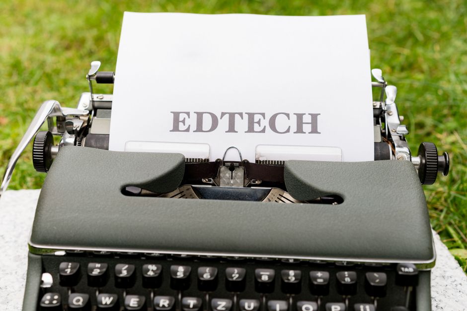 A vintage typewriter displays 'EdTech' on paper, set outdoors on grass.