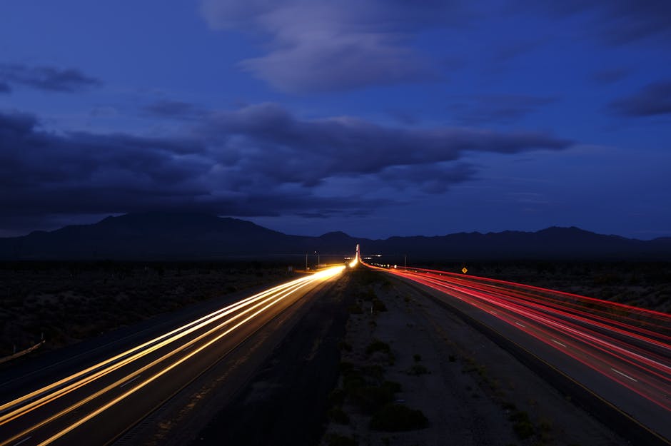 A long exposure of a highway at night showcasing dynamic light trails under a cloudy sky.