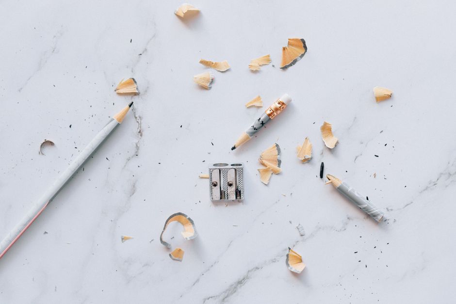 Flat lay of pencils with shavings and sharpener on a marble surface. Artistic and educational concept.