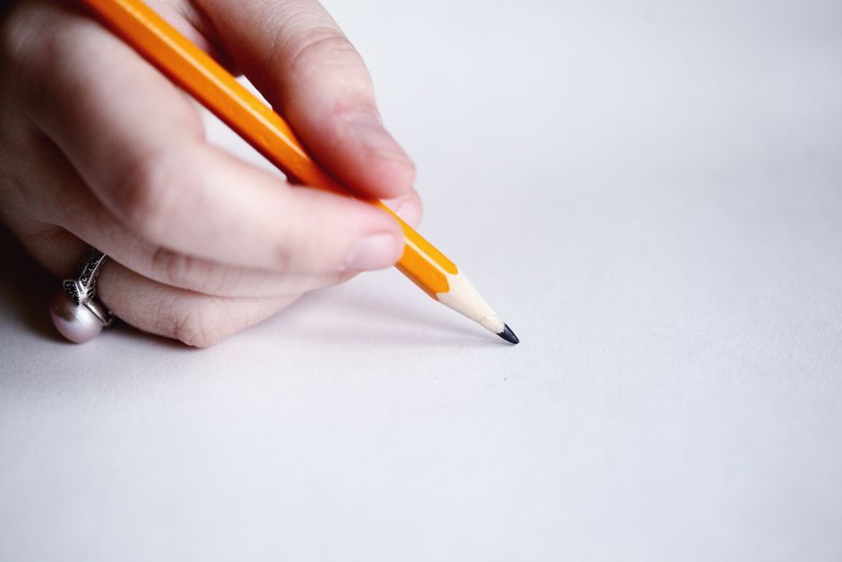 Close-up of a hand holding an orange pencil poised on blank paper, ready to write.