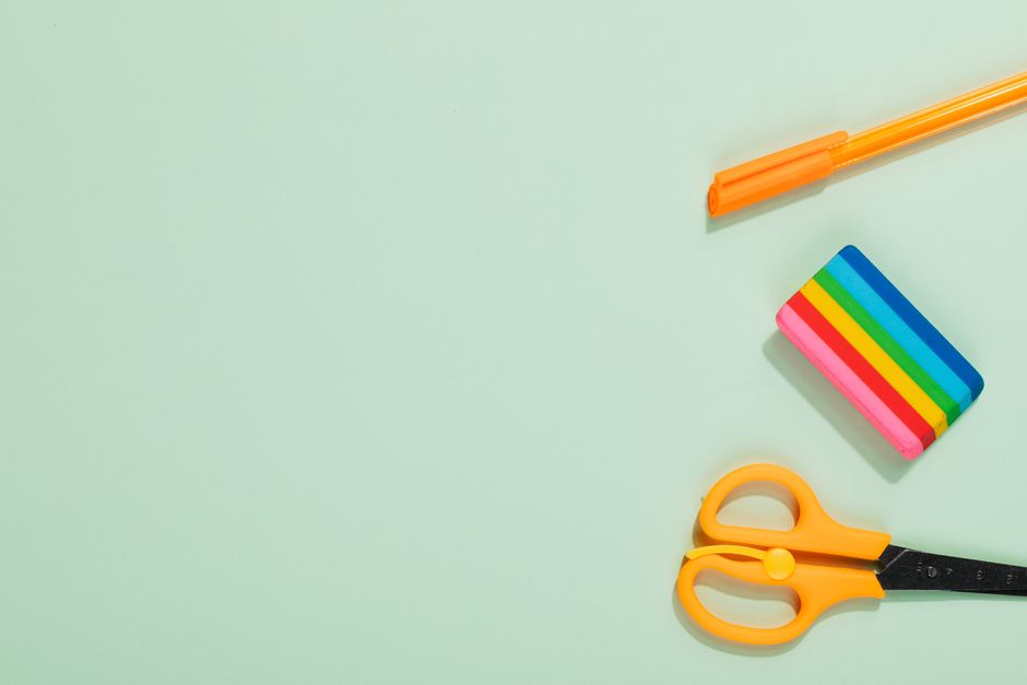 Flat lay of colorful office supplies including pen, eraser, and scissors on a pastel green background.