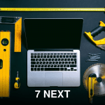 Overhead view of a laptop surrounded by various hand tools on a dark background, representing technology and construction.