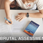 Student writing test using paper and Oxford dictionary on desk in classroom