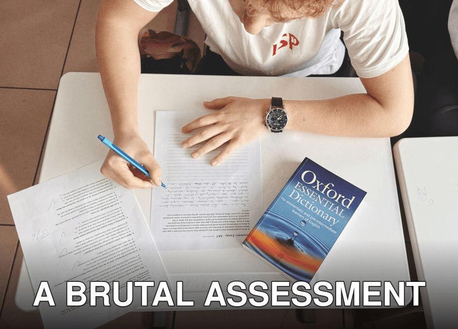 Student writing test using paper and Oxford dictionary on desk in classroom