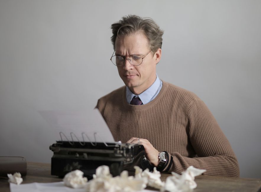 A writer concentrating while typing on a vintage typewriter indoors, surrounded by crumpled paper.