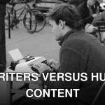 A man typing on a typewriter outdoors in a bustling street scene in England.