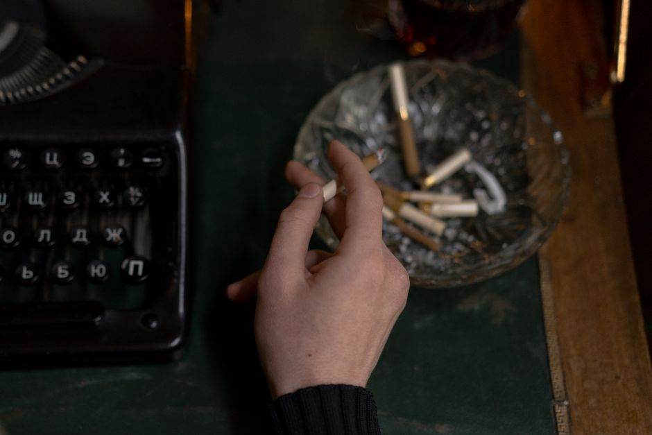 Close-up of a hand holding a cigarette near a vintage typewriter and ashtray, evoking creative inspiration.