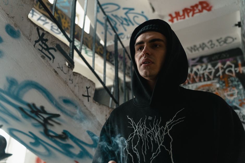 Person wearing a black hoodie stands by graffiti-covered stairs