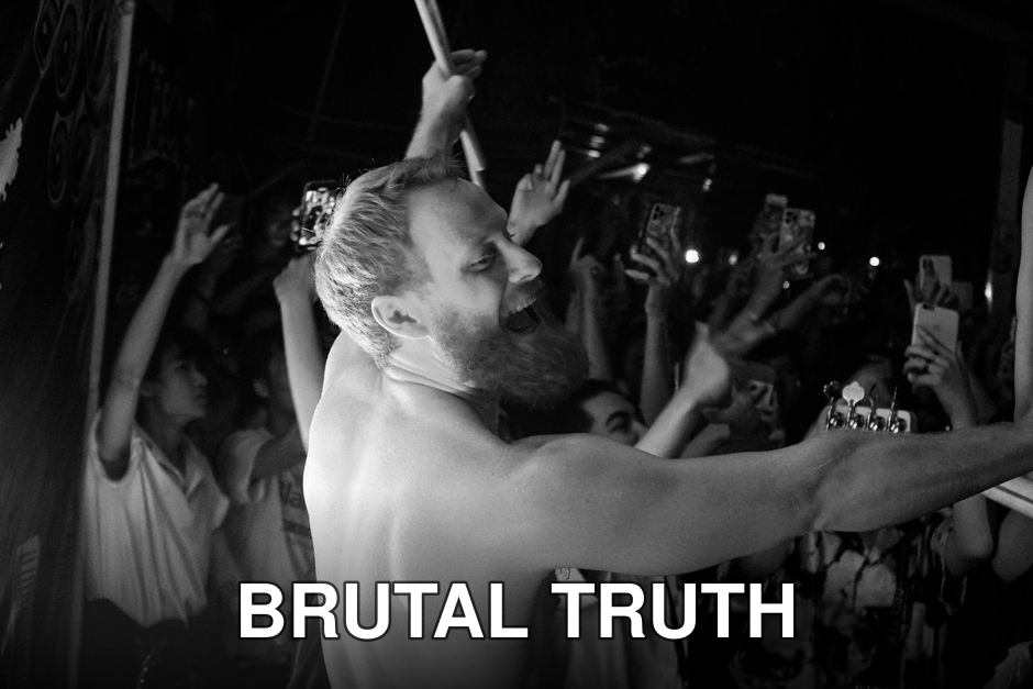 Black-and-white photo of a lively shirtless performer on stage with an enthusiastic crowd.