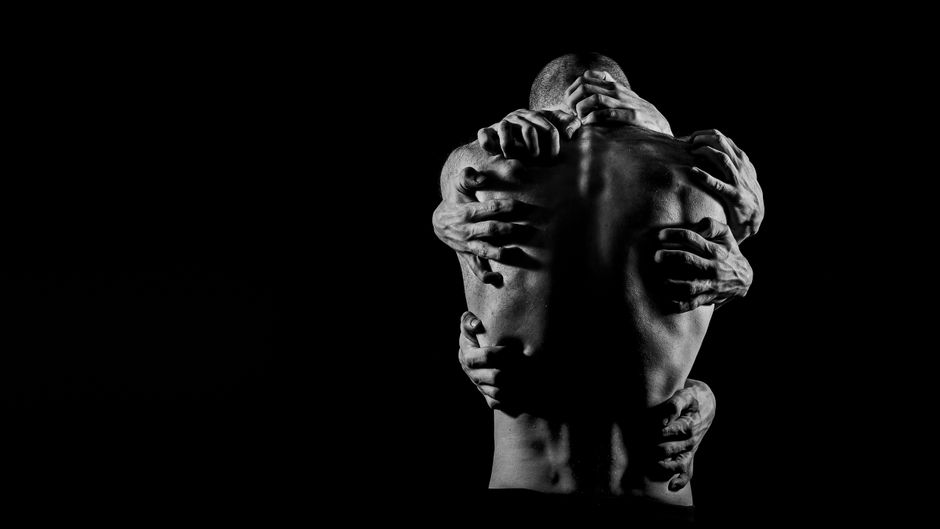 A powerful black and white image depicting multiple hands grasping a man's bare back, symbolizing complex emotions.