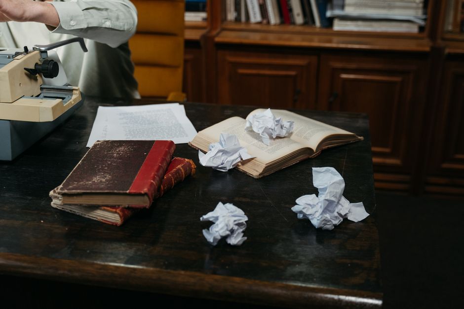 A cozy workspace with typewriter, open books, and crumpled papers on a wooden desk, perfect for creative inspiration.