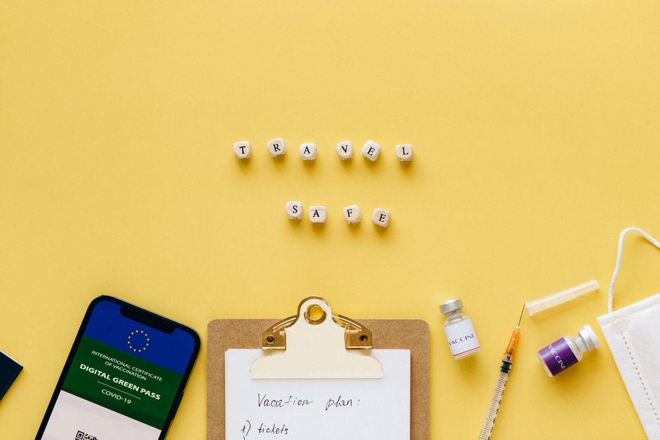 Flat lay showing travel safety essentials like a digital green pass, vaccine, and mask.