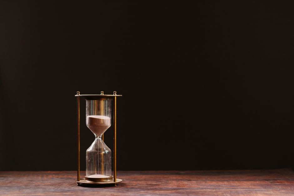 A classic hourglass with sand trickling down, symbolizing the passage of time, against a dark background.