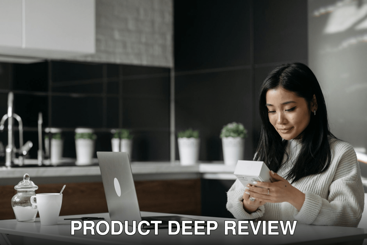 Asian woman browsing a product box while working on a laptop in a modern kitchen setting.