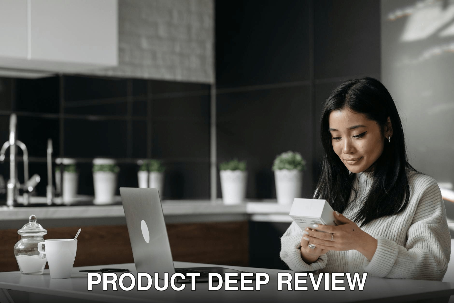 Asian woman browsing a product box while working on a laptop in a modern kitchen setting.
