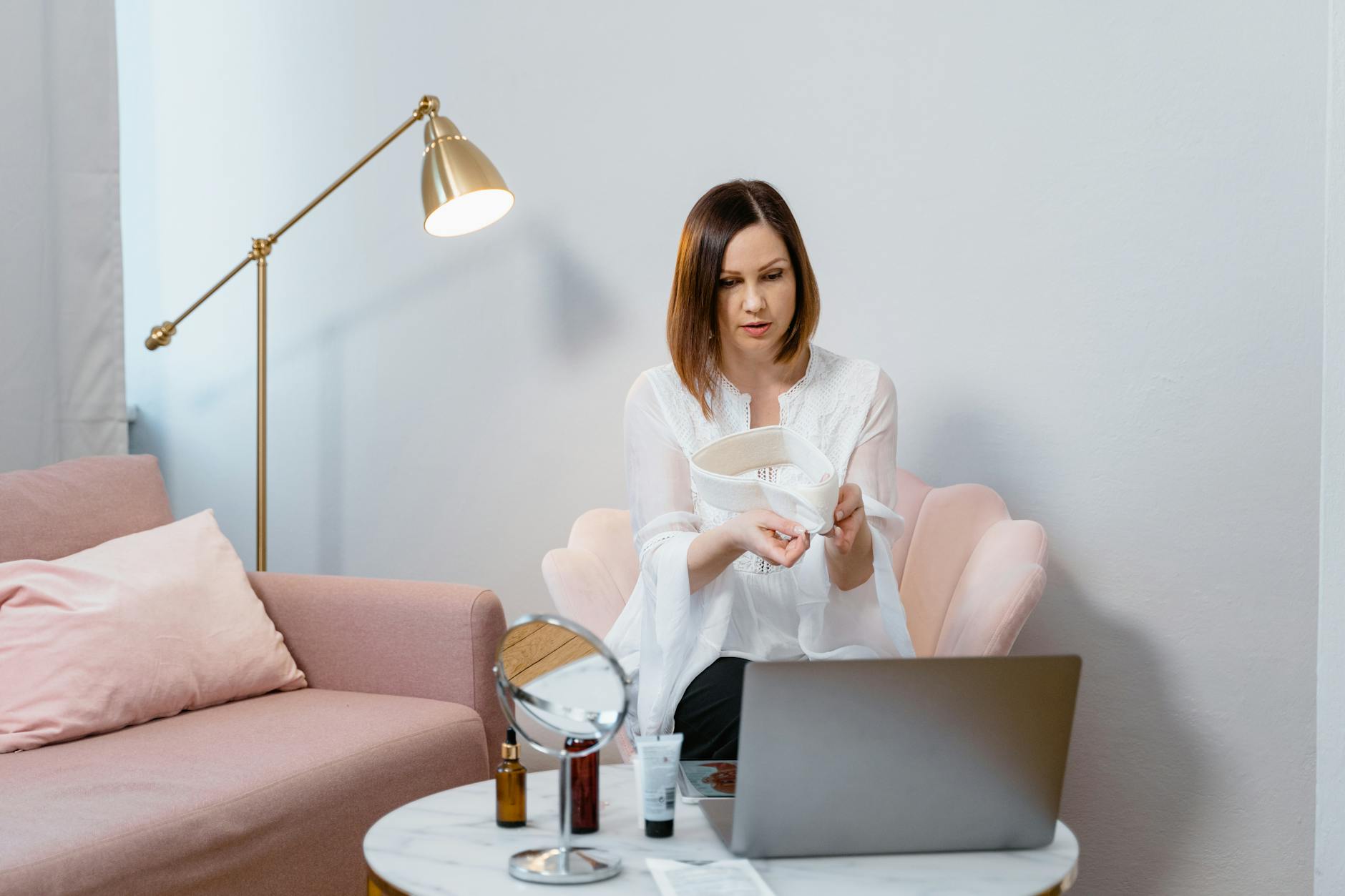 Woman in white blouse demonstrates skincare products during video call.