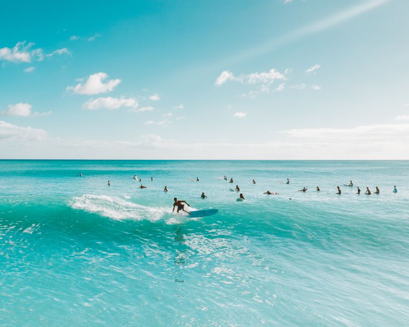 Surfers catch waves under a bright blue sky in Hawaii, reflecting ocean living and adventure.