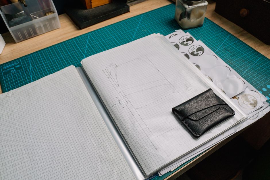 A creative workspace featuring a grid notebook, leather wallet, and various tools.