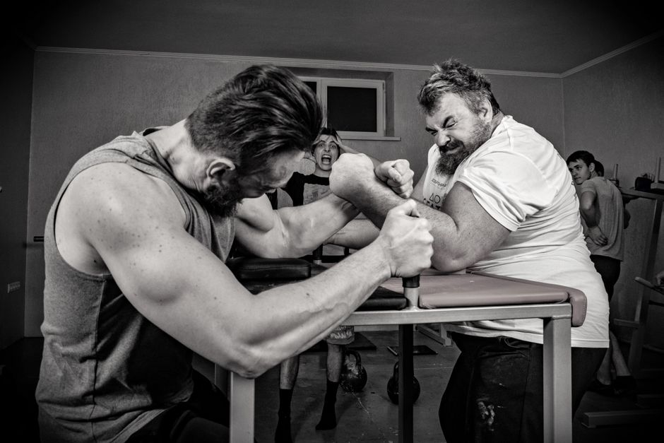 Dramatic black and white arm wrestling scene with muscular men indoors.