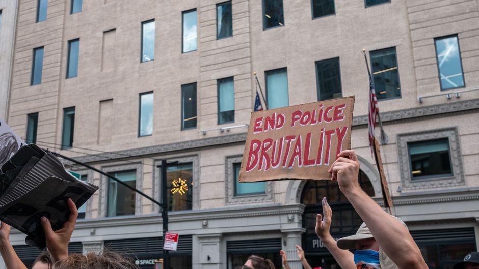 A peaceful protest with participants holding signs against police brutality in a city location.