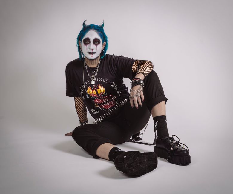 Unique emo fashion portrait featuring blue hair and bold makeup against a neutral studio backdrop.