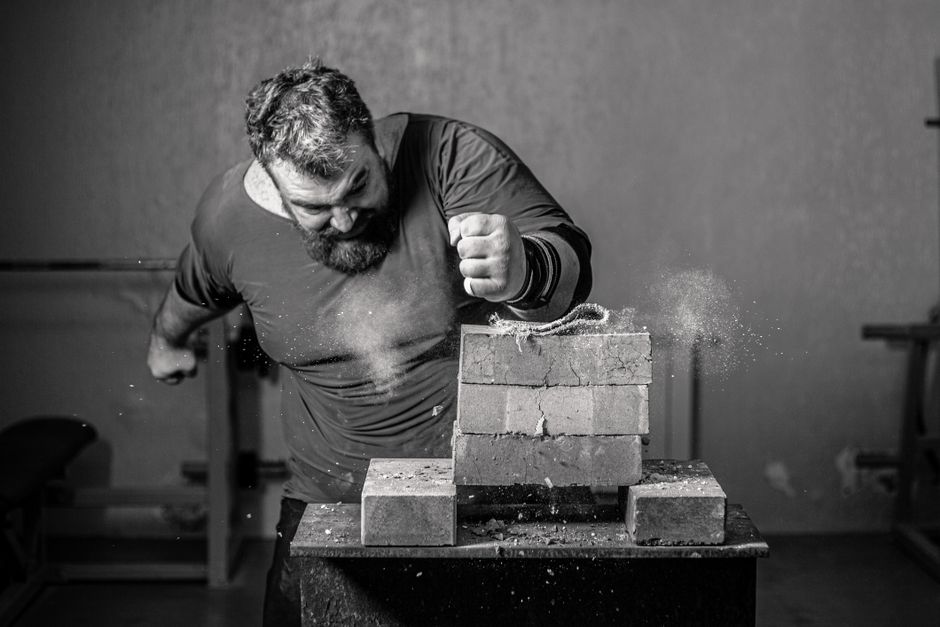 Dramatic grayscale image of a man breaking bricks indoors with powerful force.