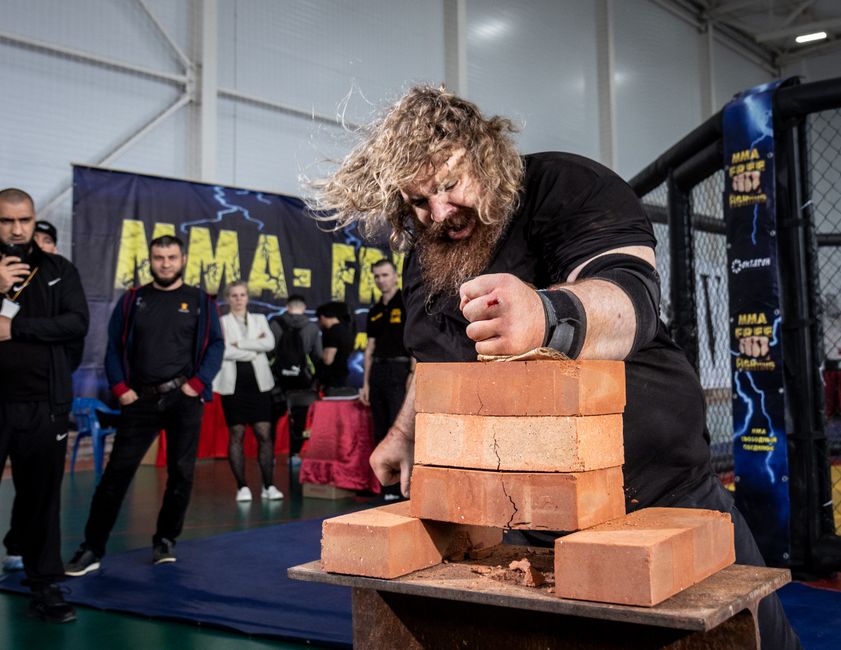 A strongman breaks bricks in an impressive display of power during a competition indoors.