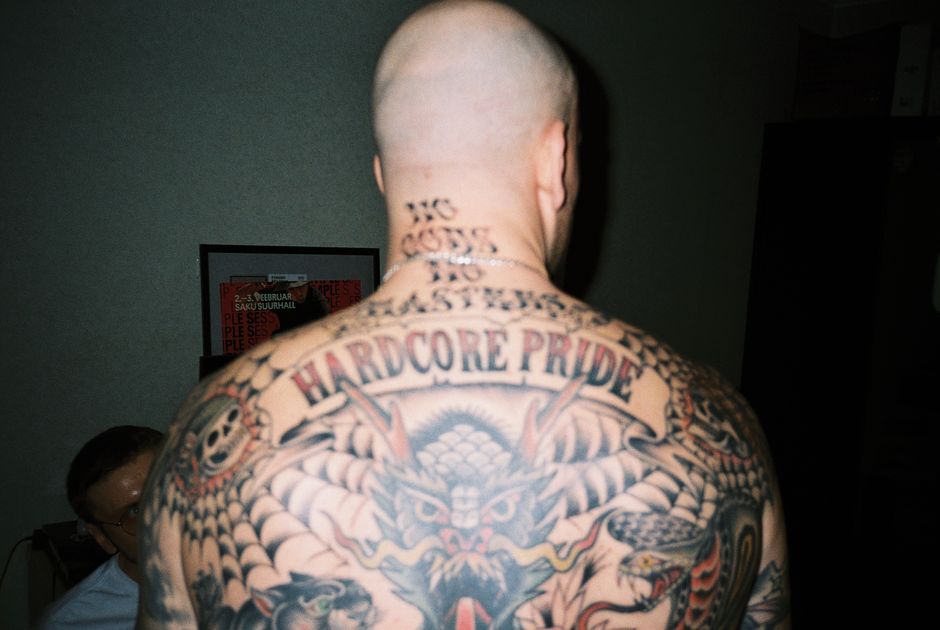 Bald man with intricate tattoos on back, vibrant tattoo art displayed indoors.