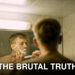 Adult man shaving in a bathroom mirror, highlighting daily grooming routine.