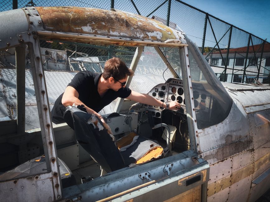 Man investigates controls inside an old airplane cockpit under bright daylight.
