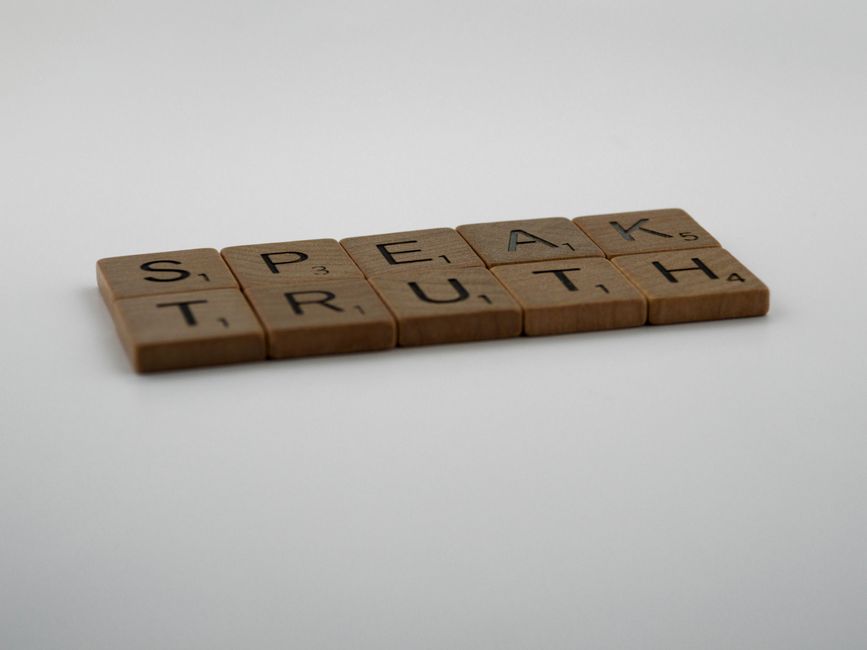 Wooden Scrabble tiles forming the phrase 'Speak Truth' on a white surface.