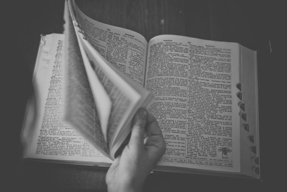 A black and white close-up of a hand flipping through an open dictionary.