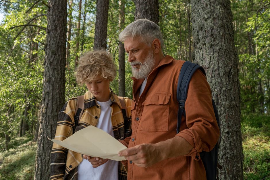 Grandfather and grandson navigate with a map while hiking in a lush forest.