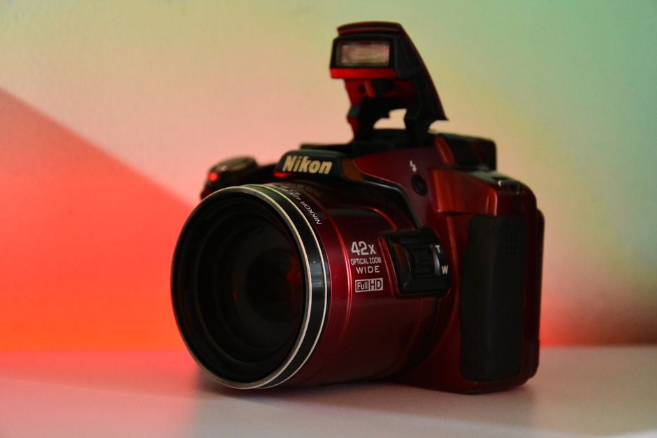 Close-up of a vibrant red digital camera with a pop-up flash against colorful studio lighting.