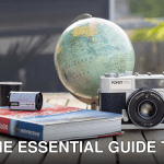 A vintage camera with a globe and book on a wooden table, ideal for travel and photography themes.