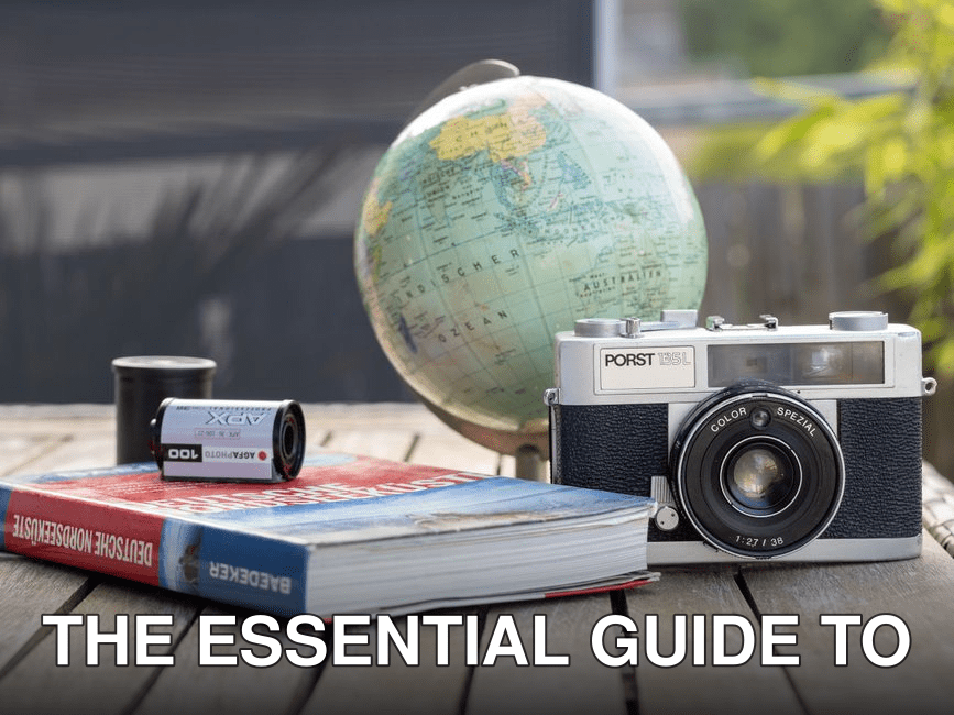 A vintage camera with a globe and book on a wooden table, ideal for travel and photography themes.