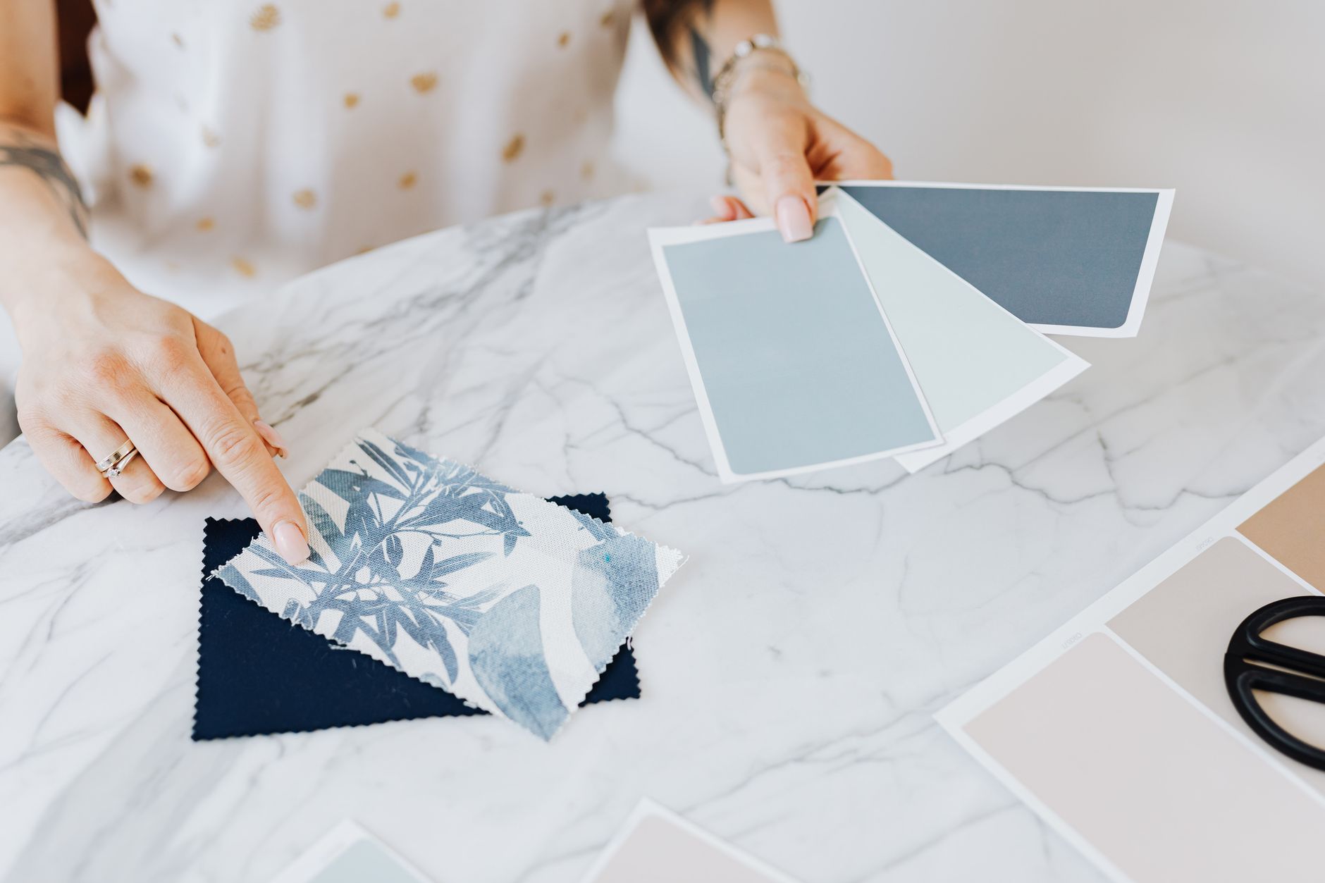Woman selecting color and fabric swatches on marble desk for interior design project.