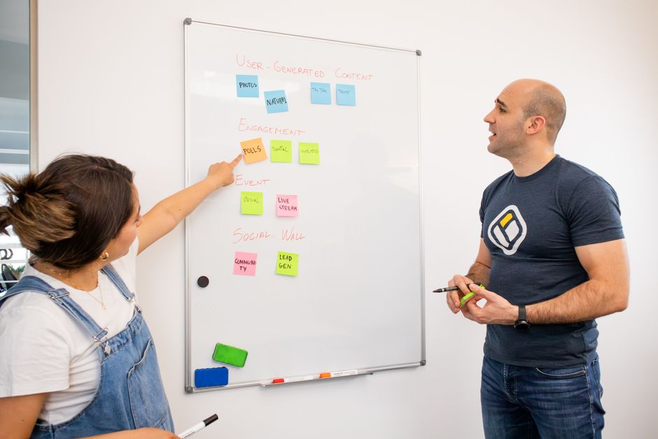 Two colleagues brainstorm on a whiteboard with colorful sticky notes for project planning.