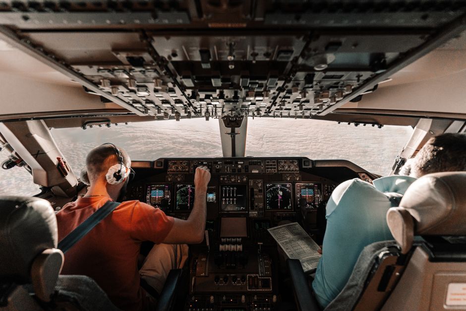 Pilots navigating a commercial plane cockpit with daytime views outside.