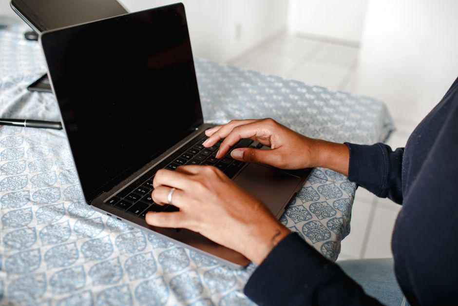 Close-up of hands typing on a laptop indoors on a patterned tablecloth.