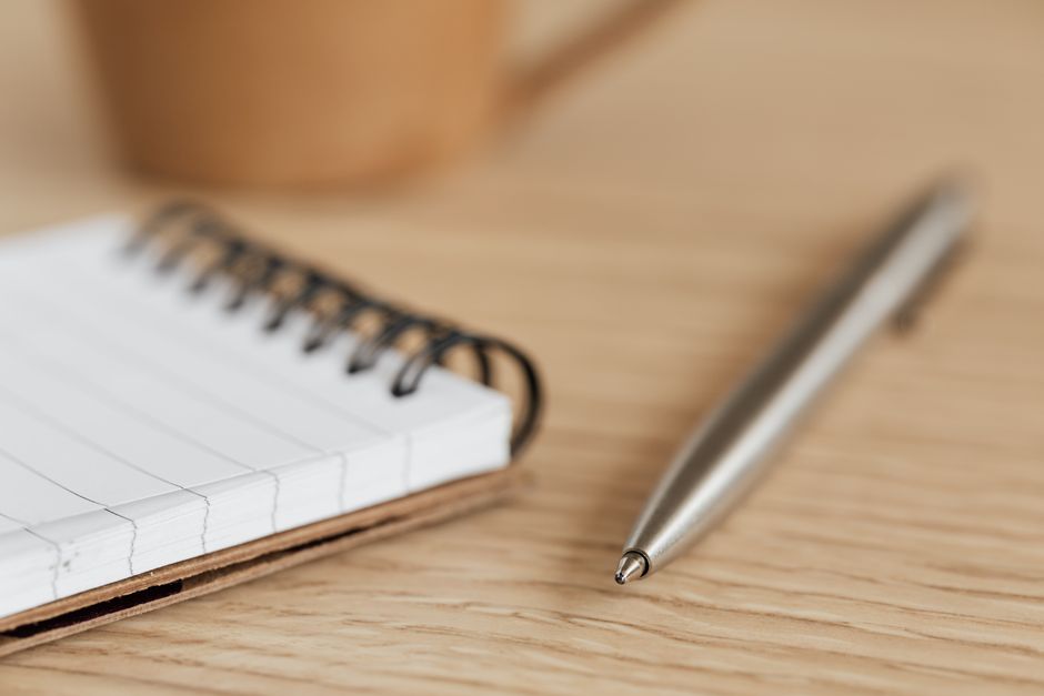 A detailed close-up photograph of a notepad and pen resting on a wooden desk.