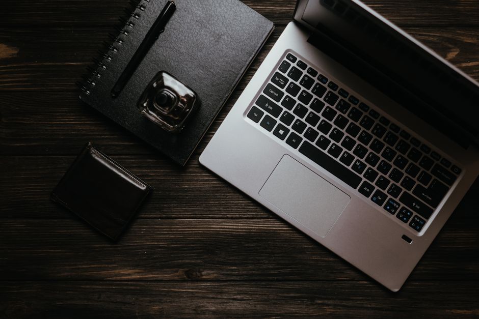 Flat lay of a laptop, notebook, pen, and wallet on a wooden table.