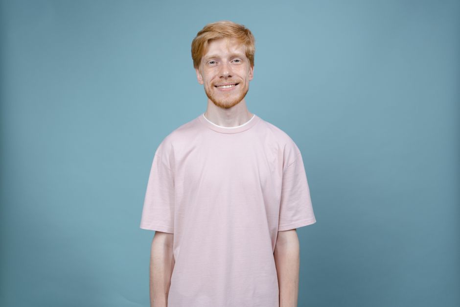 A cheerful man with blonde hair wearing a pastel shirt against a blue background.