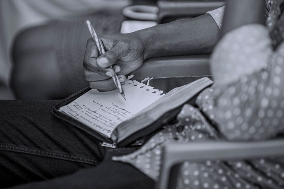 Black and white photo capturing a person writing notes in a notebook, focusing on the hand and pen.