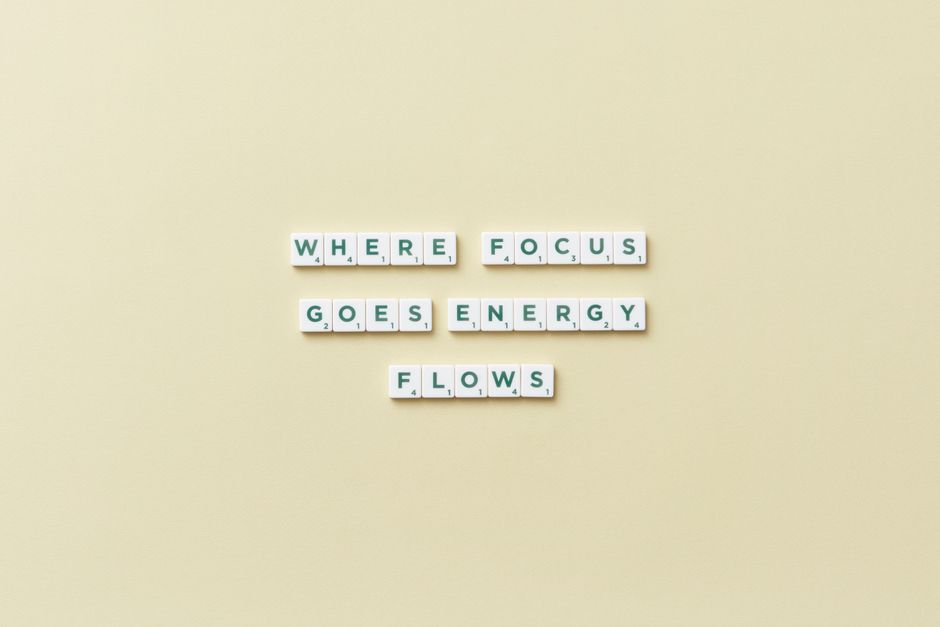 Inspirational quote 'Where Focus Goes Energy Flows' spelled with Scrabble tiles on a minimalist background.