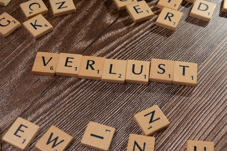 Scrabble tiles spelling 'Verlust' on a wooden table, symbolizing loss or financial context.